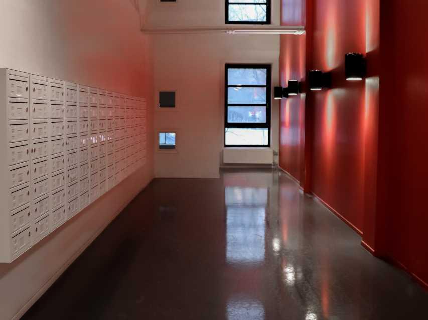 Postkasser i oppgang Kompakt fra Stansefabrikken, sorte vegglys på rød vegg, vindu i enden av veggen FOTO